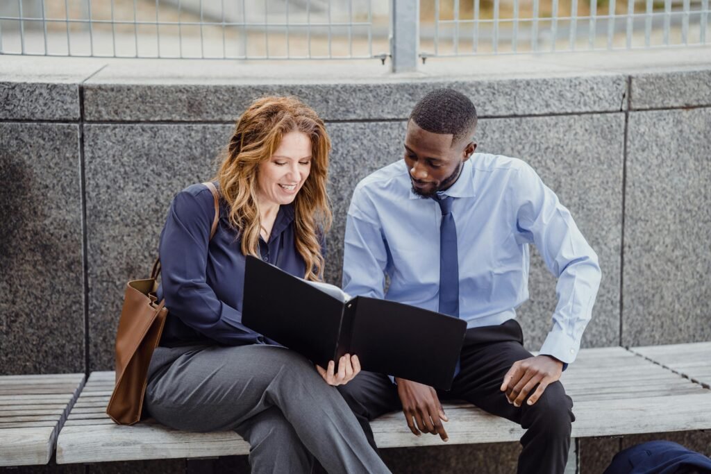 Two colleagues discussing a document while seated on an outdoor bench, showcasing teamwork.
